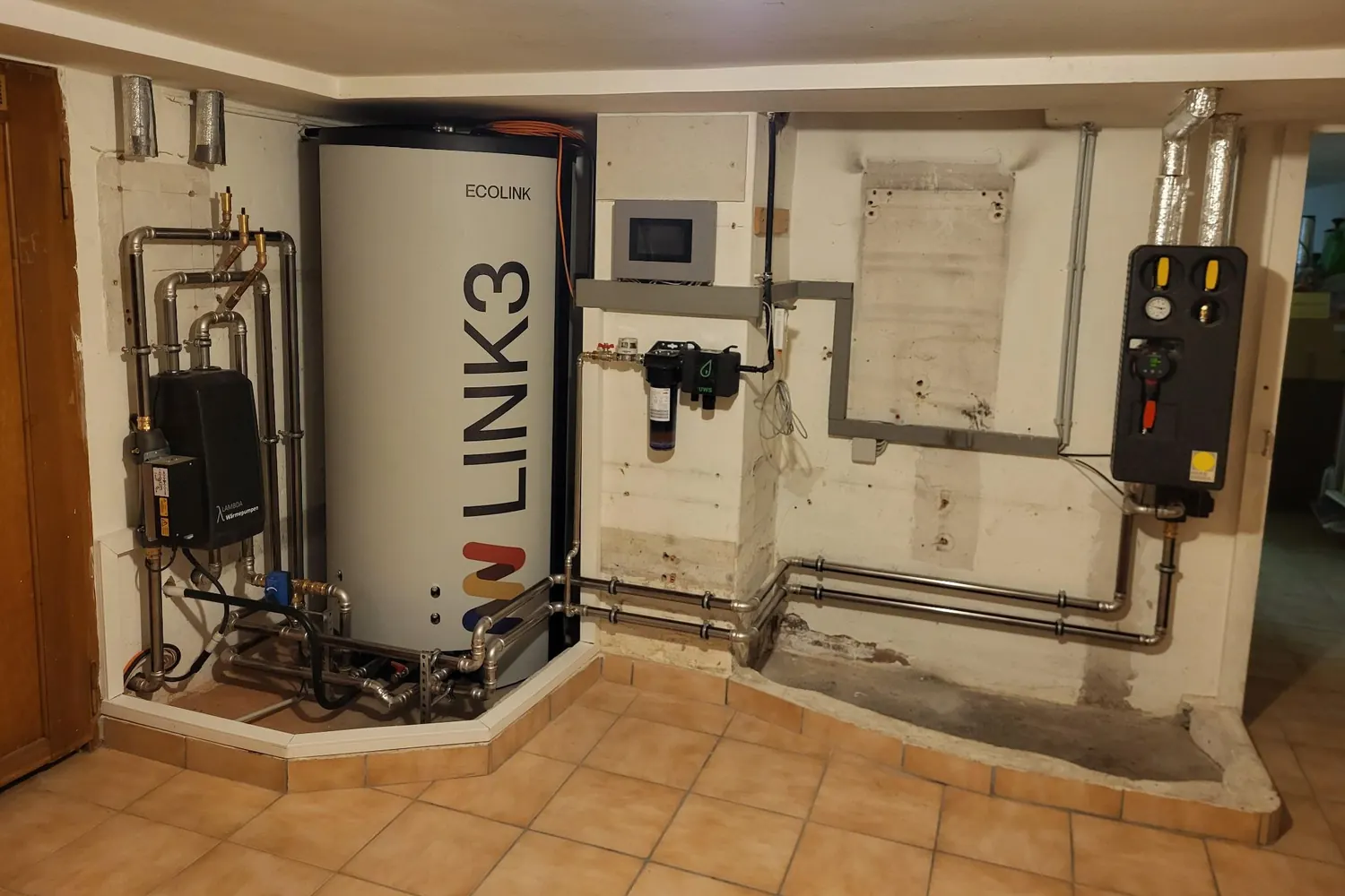 Heizraum nach dem Umbau: links das Innengerät der Wärmepumpe, daneben der Speicher, in der Mitte die Regelung, rechts die Pumpengruppe des Heizkreises; an der Wand die hellen Spuren eines abgebauten Wandgeräts