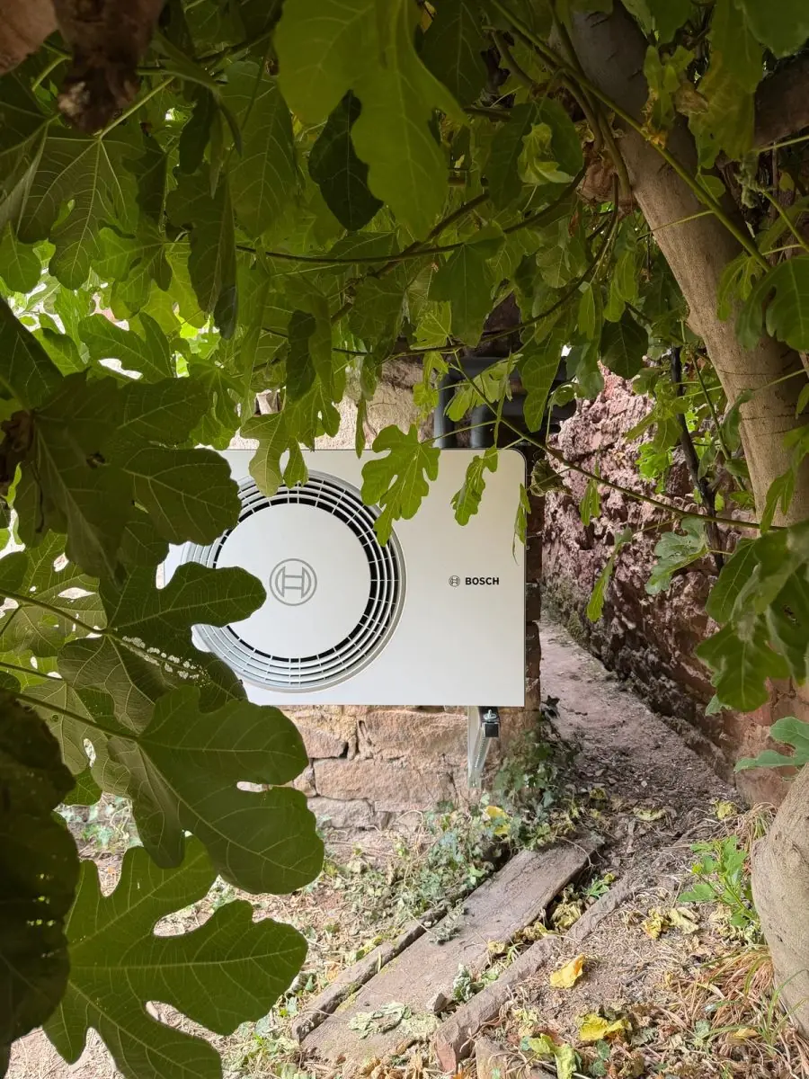 Außeneinheit einer Bosch-Wärmepumpe hinter den Blättern eines Feigenbaums; Luft-/Wasser-Wärmepumpe in Weyher in der Pfalz